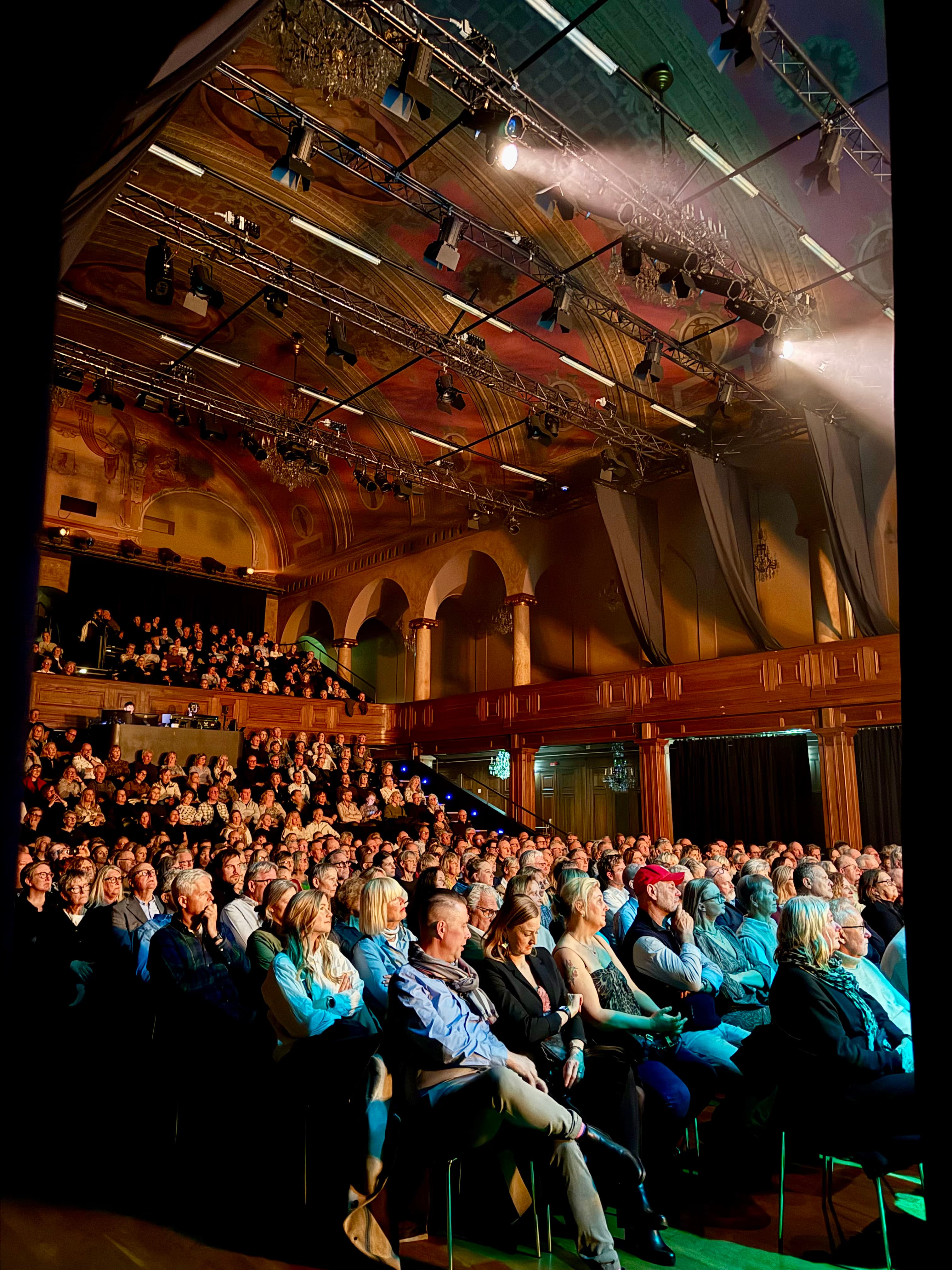 Full Main Hall with audience in the stalls and balcony beneath the painted ceilings