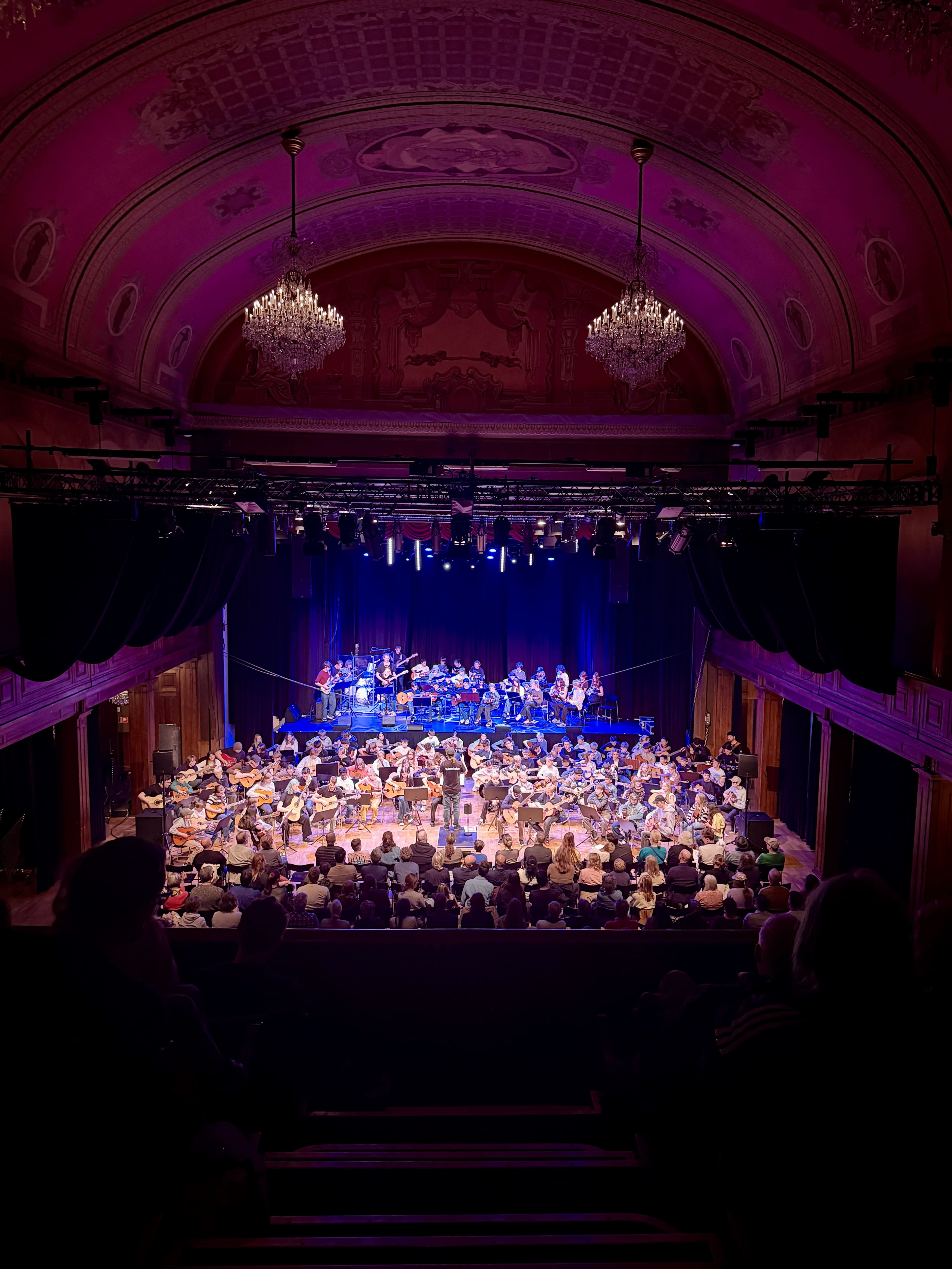Large orchestra on stage in atmospheric lighting before a seated audience