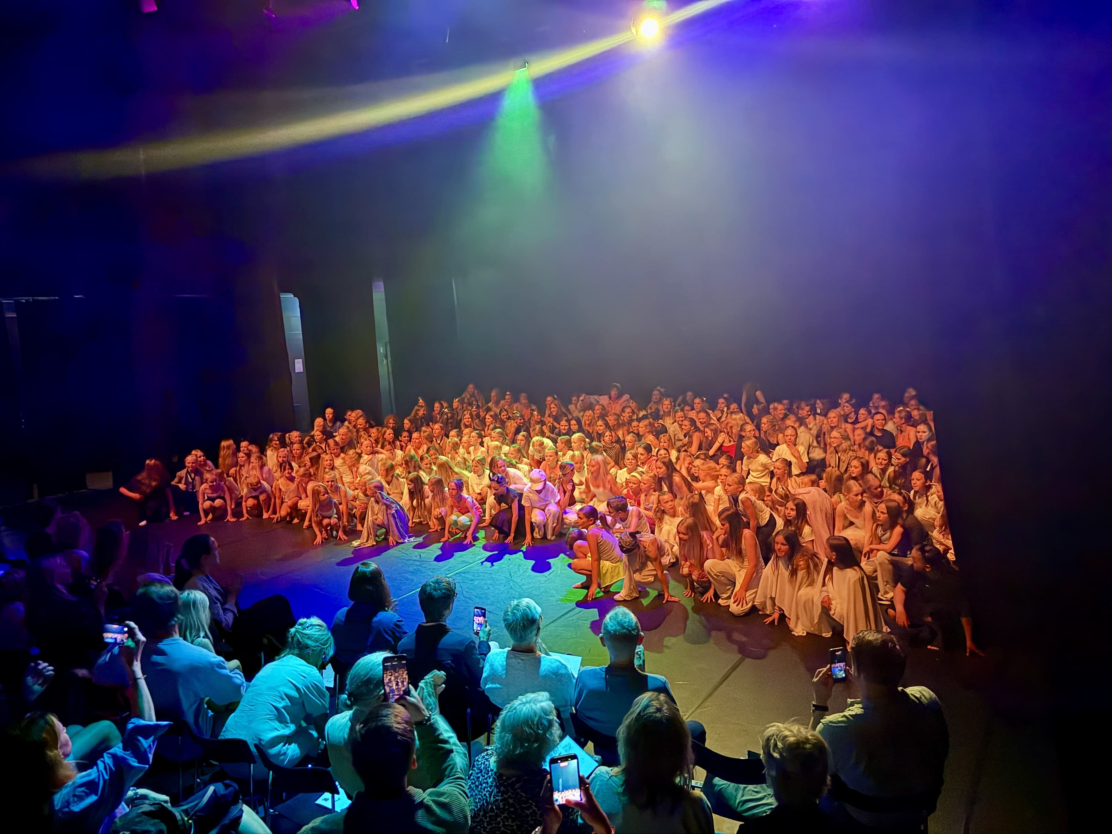 Dance performance – ensemble gathered on the stage floor in colorful lighting